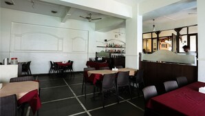 A restaurant interior with tables, chairs, a bar area, and ceiling fans. - HMR Royal Inn (Pune)