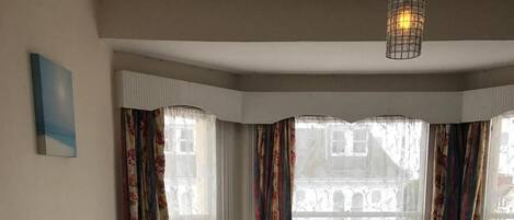 A hotel room with a large bed, two armchairs, a view of buildings through the window, and a hanging light fixture.