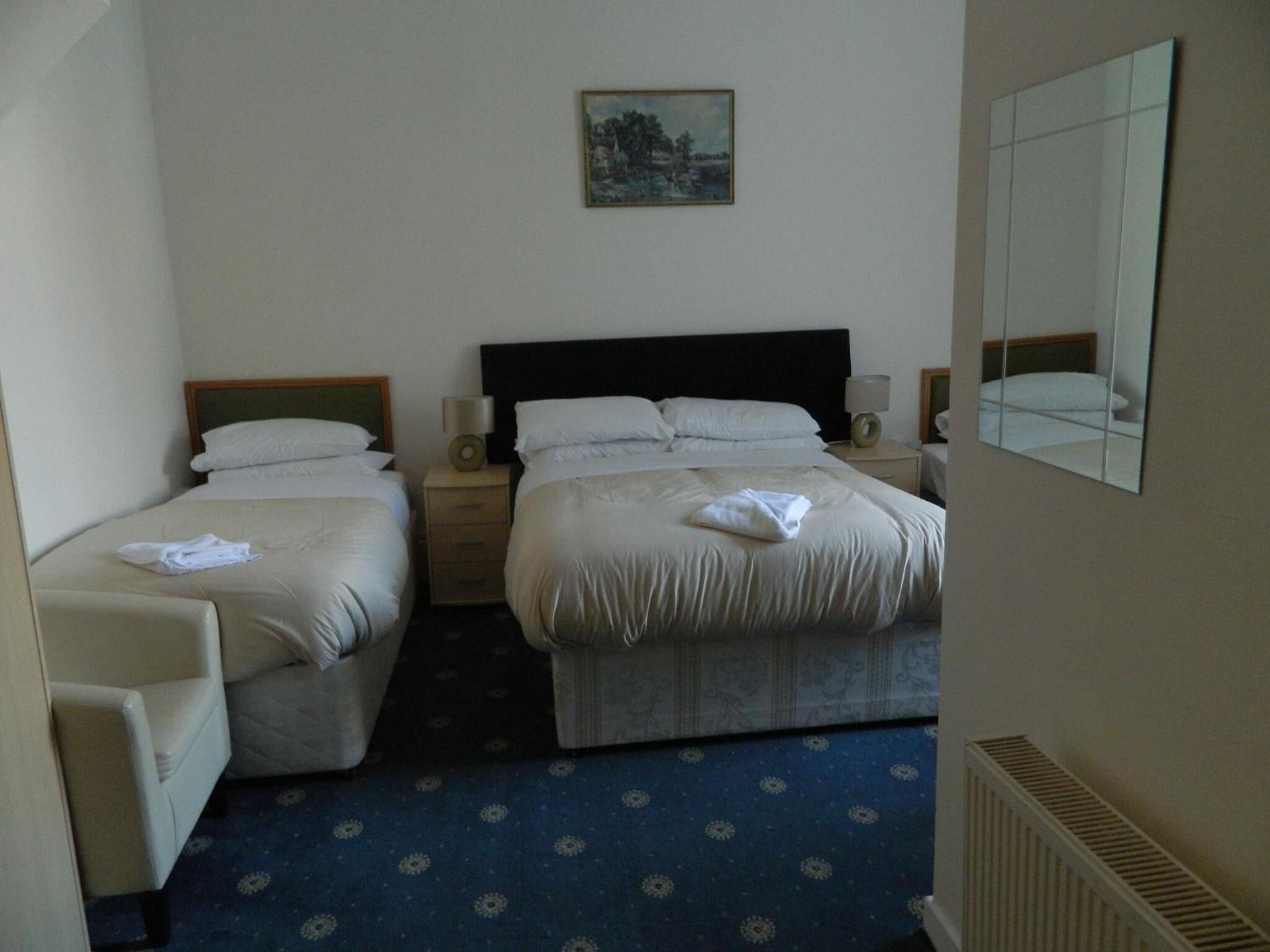 Une chambre d’hôtel avec deux lits, un petit bureau, une chaise, un tableau au mur et un miroir.