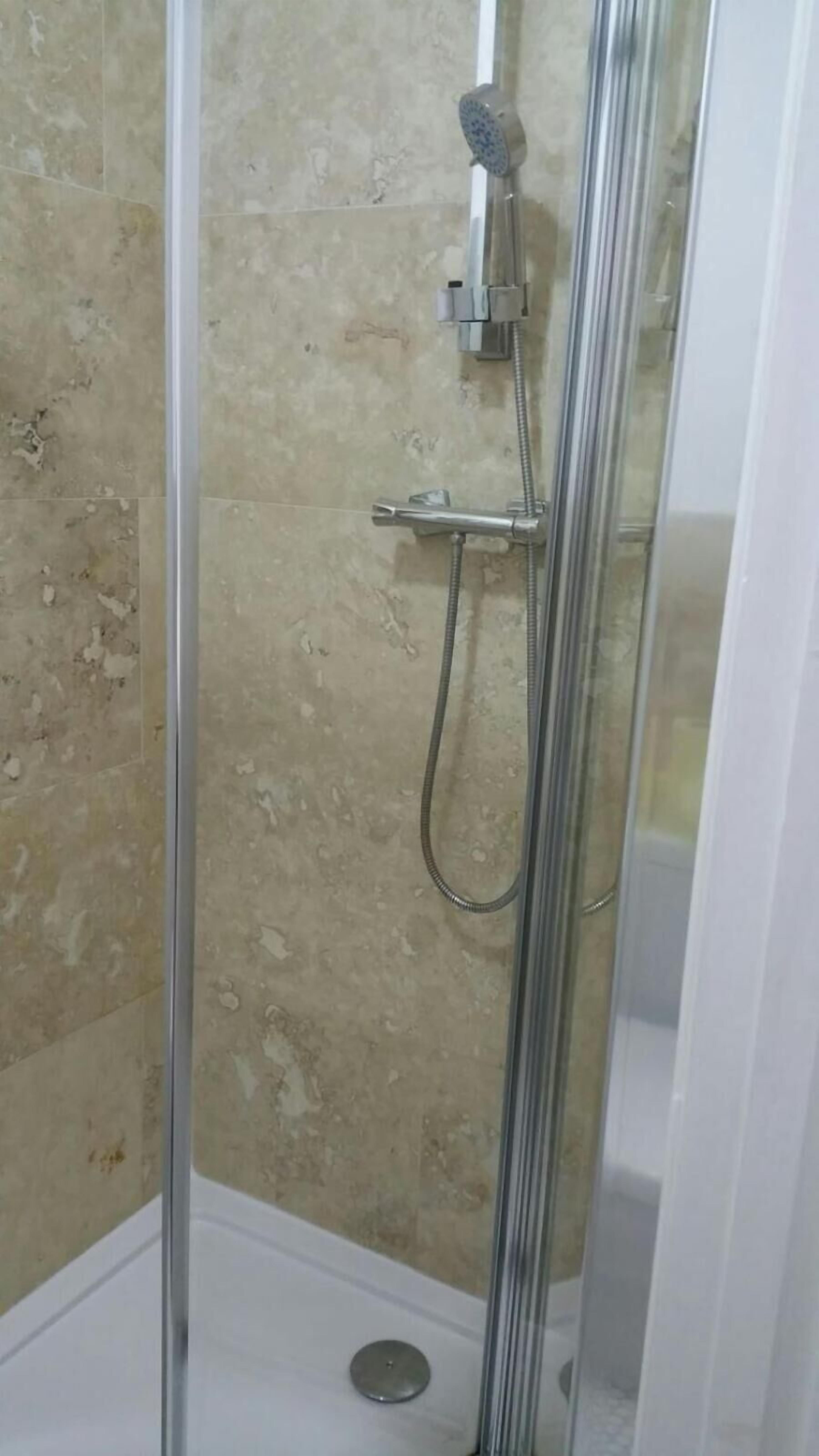A glass-enclosed shower with a handheld showerhead and a handheld faucet.