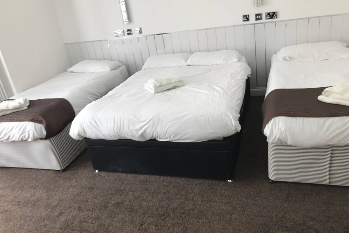 A hotel room with three single beds arranged in a row, each with white bedding and a brown throw blanket.