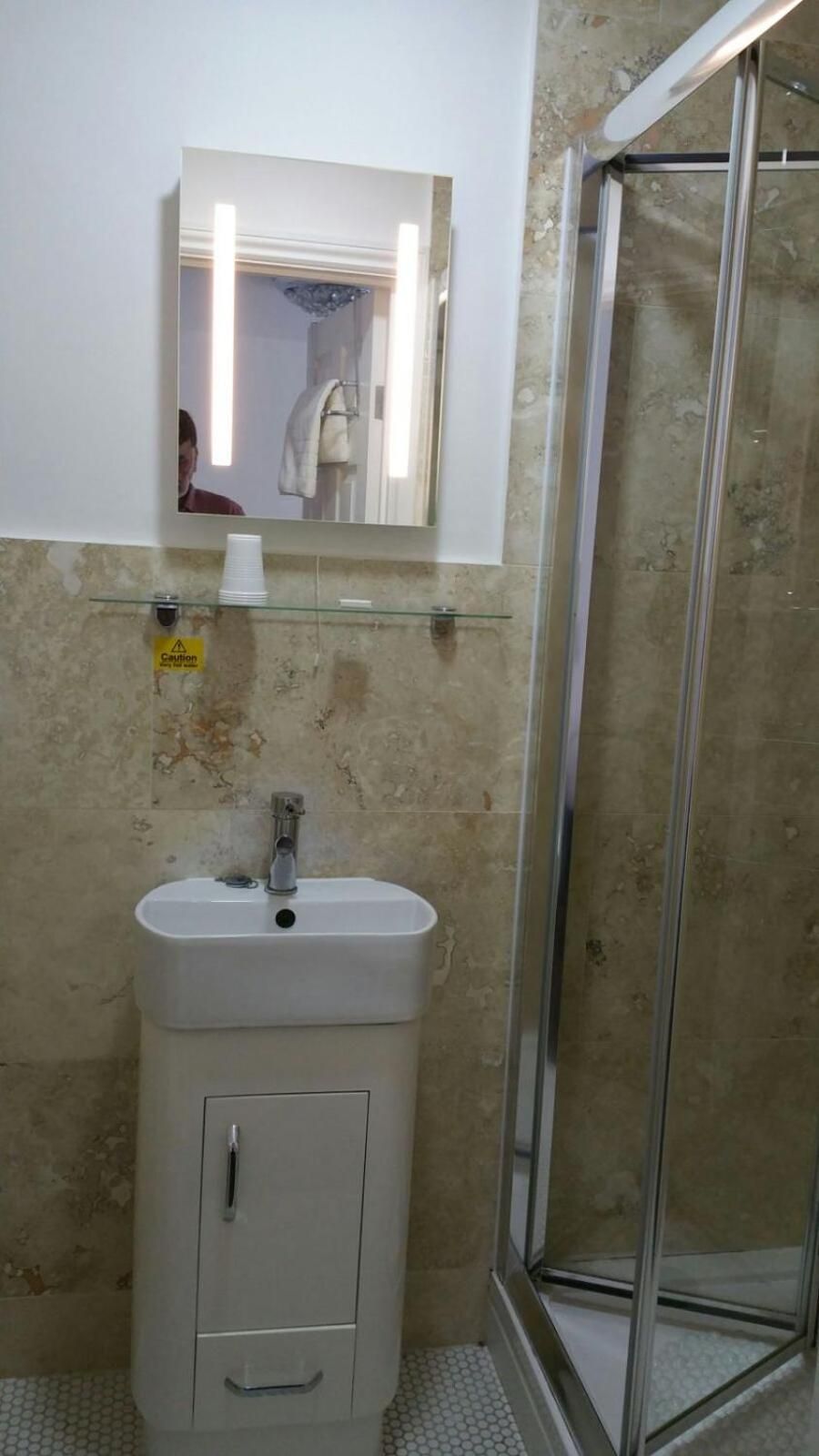 A bathroom with a glass shower enclosure, a sink with a mirror above it, and a caution sign on the wall.