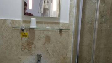 A bathroom with a glass shower enclosure, a sink with a mirror above it, and a caution sign on the wall.