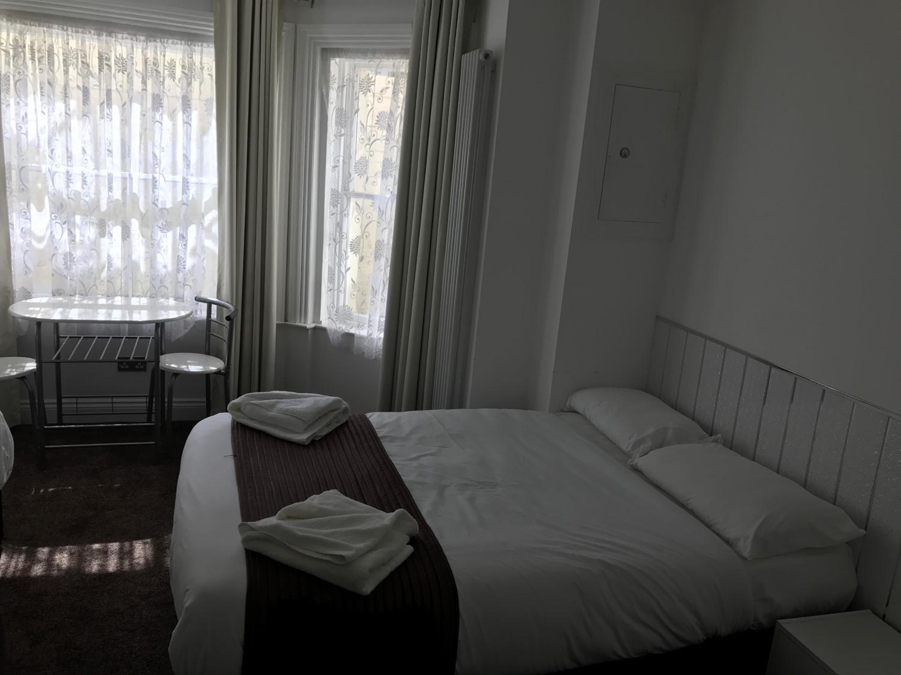 Ein Hotelzimmer mit einem Bett, einem kleinen Tisch mit Stühlen und einem Fenster mit Vorhängen.