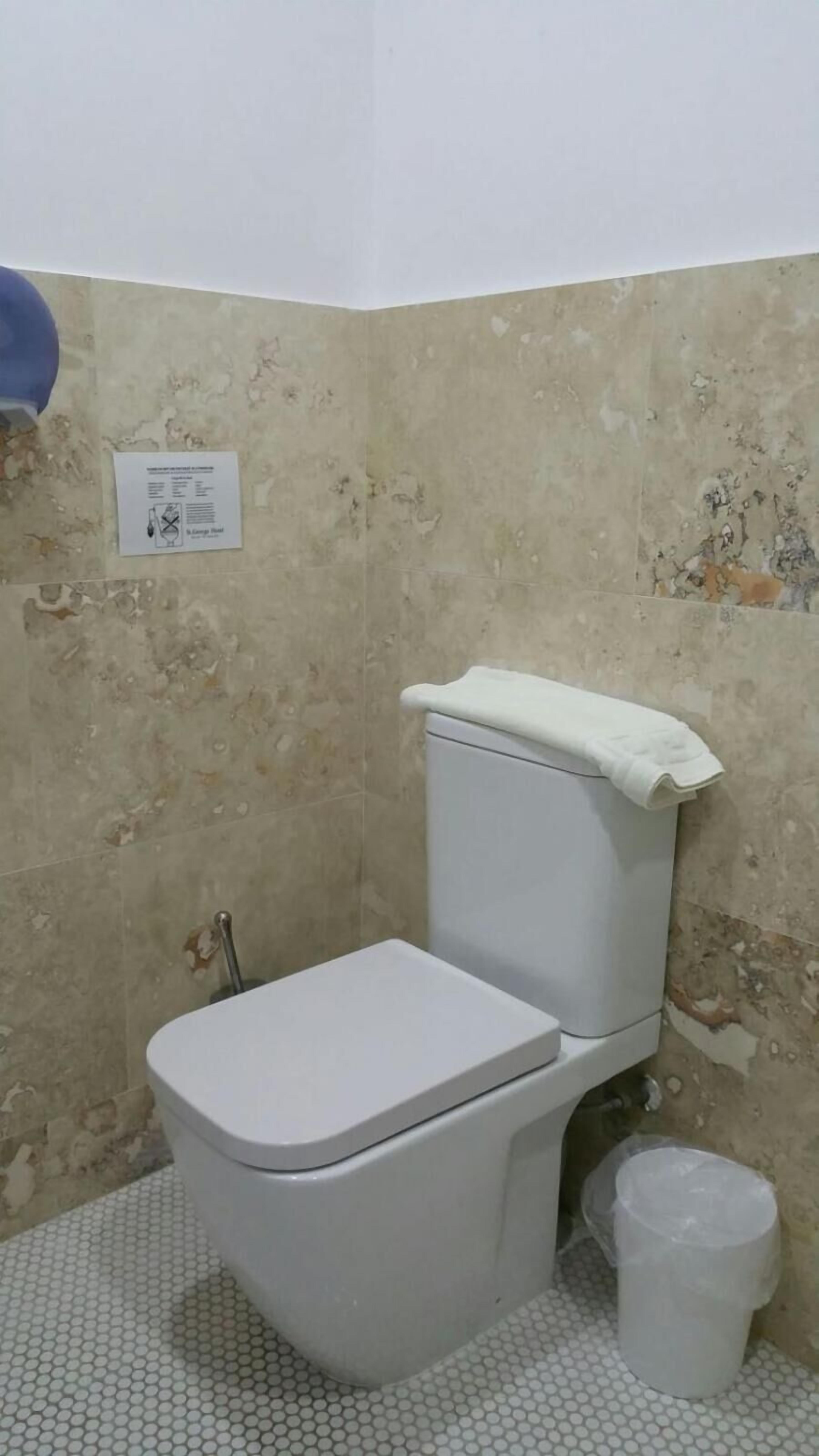 Ein kleines, schlichtes Badezimmer mit Toilette, Mülleimer und einem an der Wand befestigten Schild.