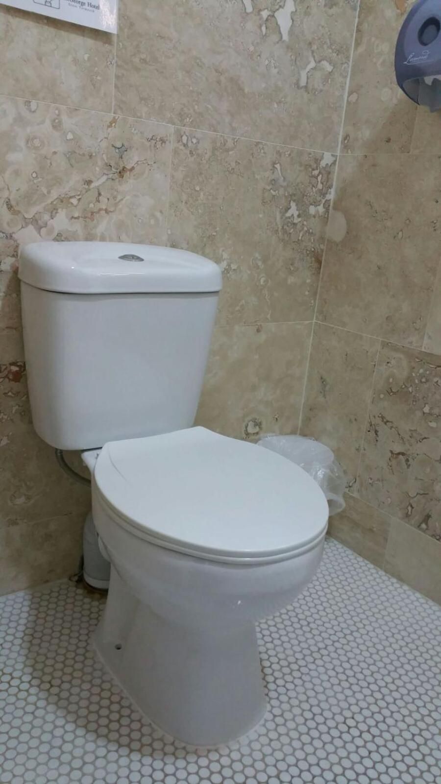 A toilet with a white seat and lid, a white trash bin, and a tiled floor with a hexagonal pattern.