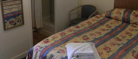 Una habitación de hotel con una cama, una silla, zona de ducha y un espejo.