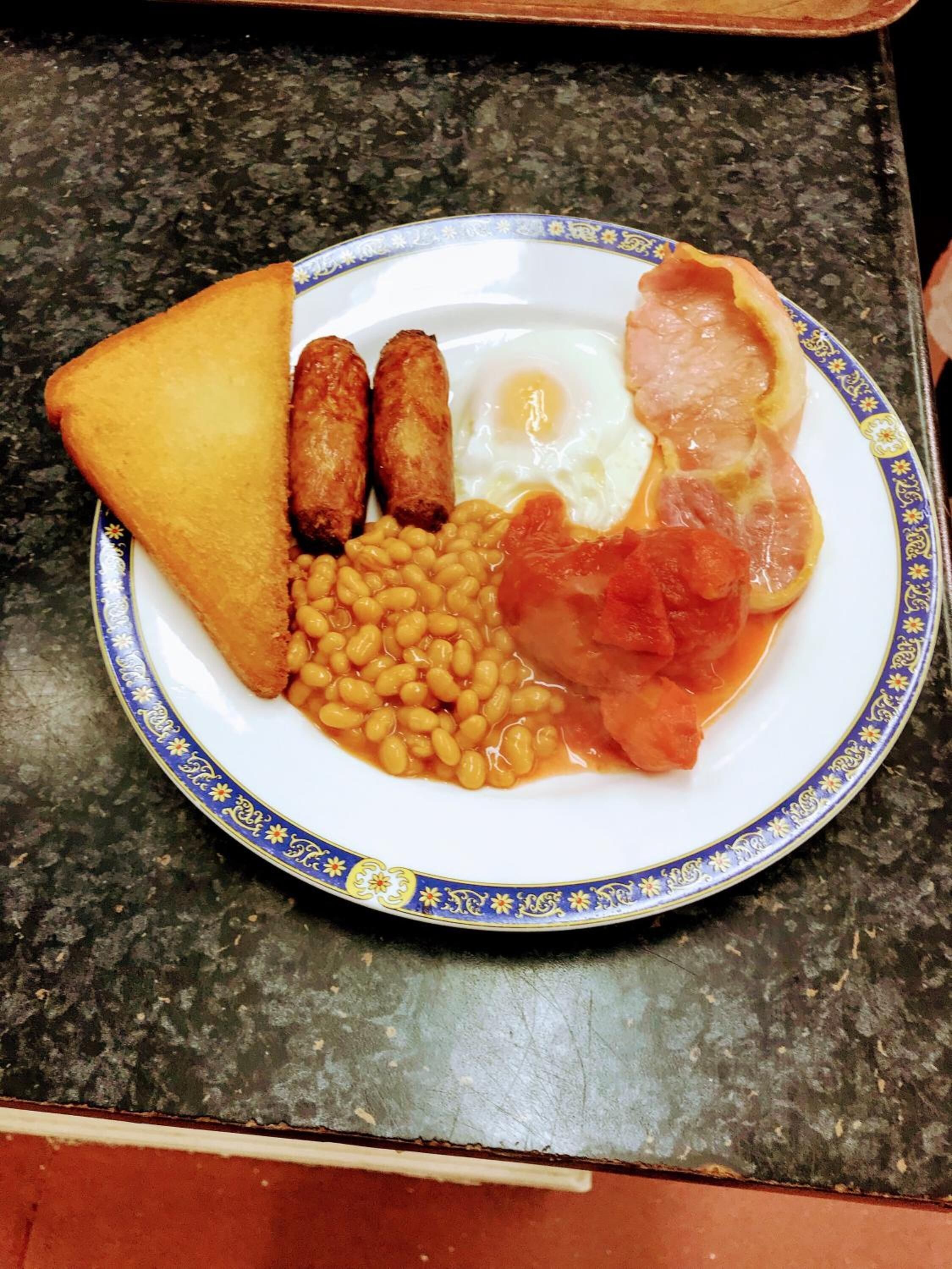 A plate of breakfast food including toast, sausages, eggs, beans, and bacon.