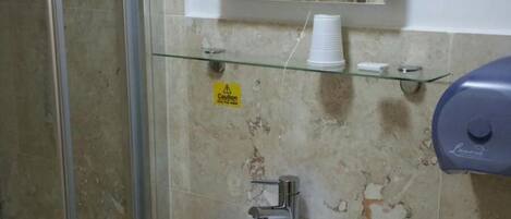 Un baño con cabina de ducha de vidrio, un lavamanos blanco y un espejo encima.