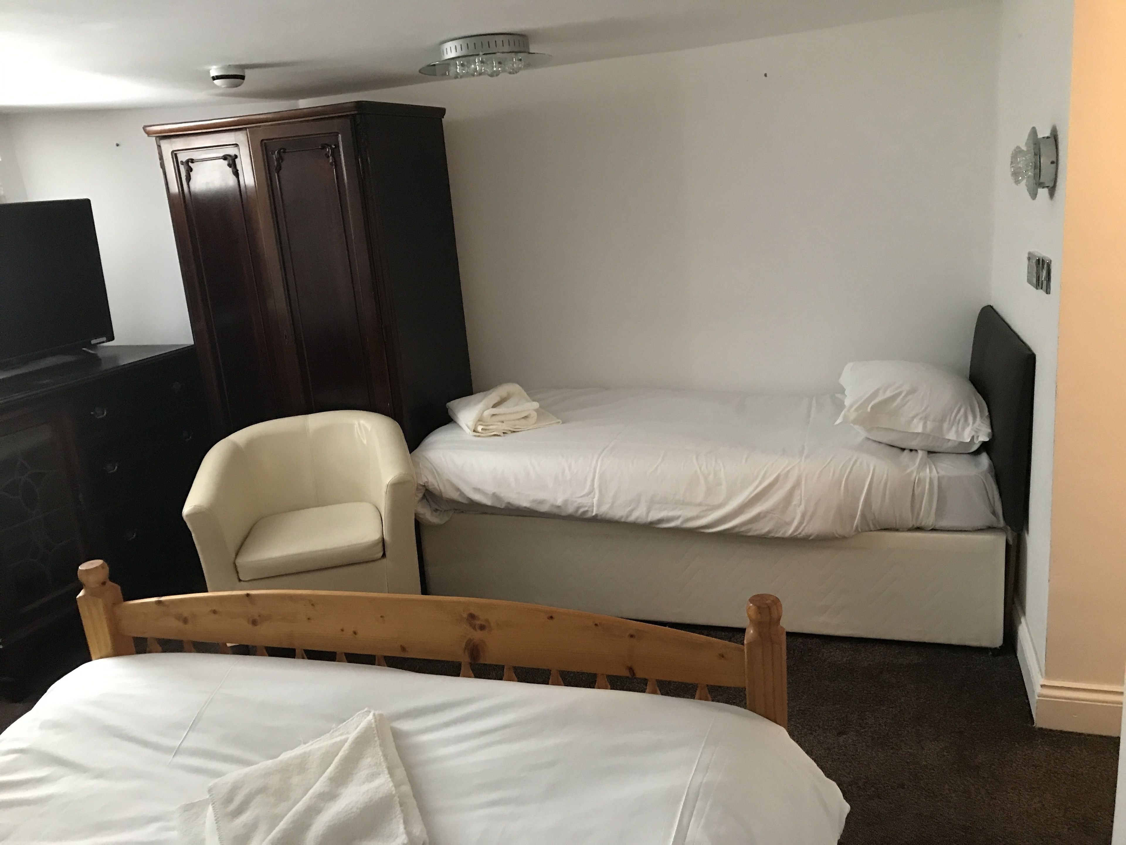 Ein Hotelzimmer mit zwei Betten, einem Holz-Kopfteil, einem Holzstuhl, einem dunklen Holzschrank und einem Flachbildfernseher.