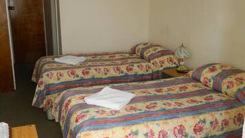 A room with two beds, a wooden table, a chair, a lamp, and a painting on the wall.