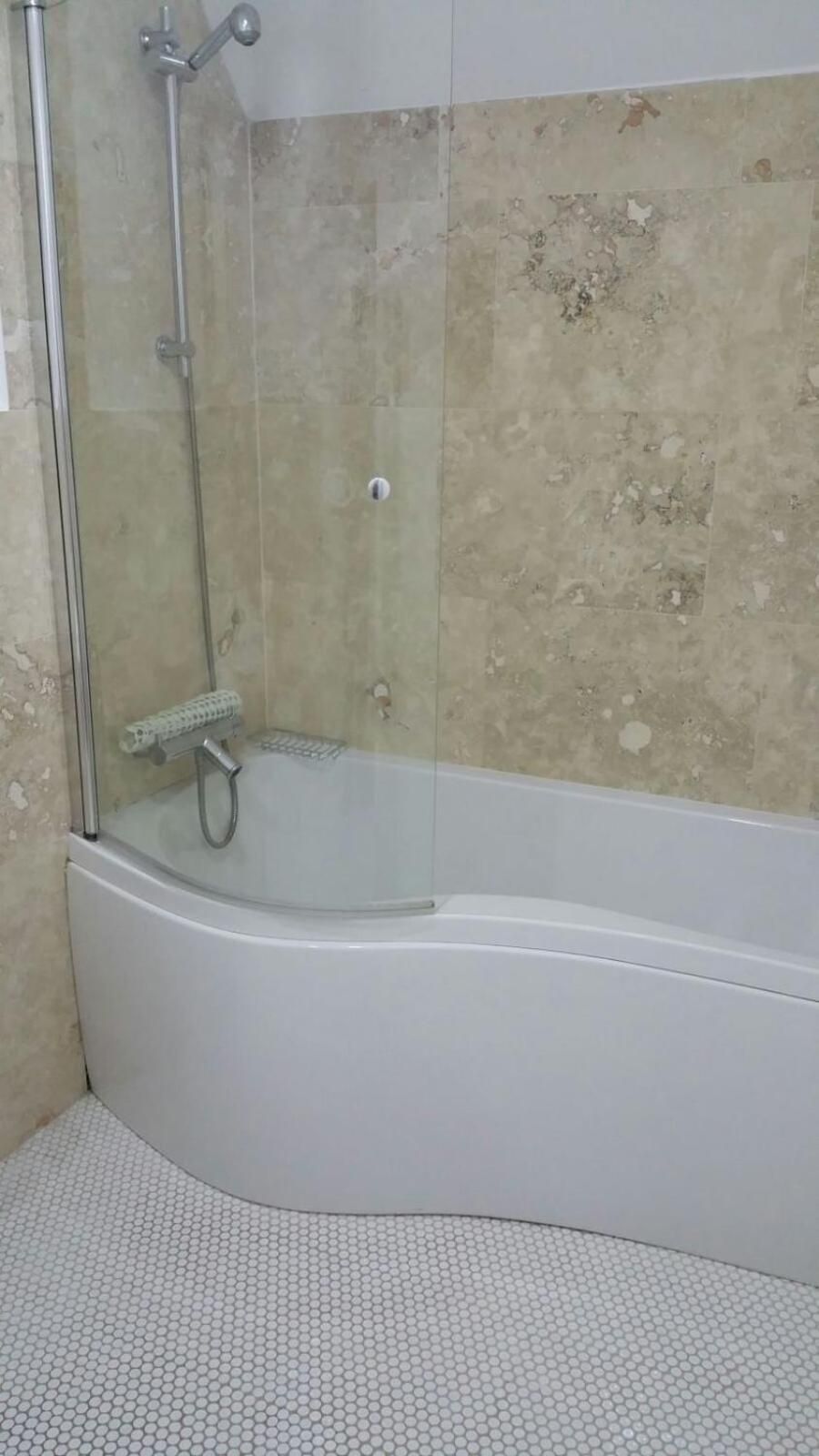 Un bagno con doccia vetrata, una vasca da bagno bianca e un pavimento piastrellato.