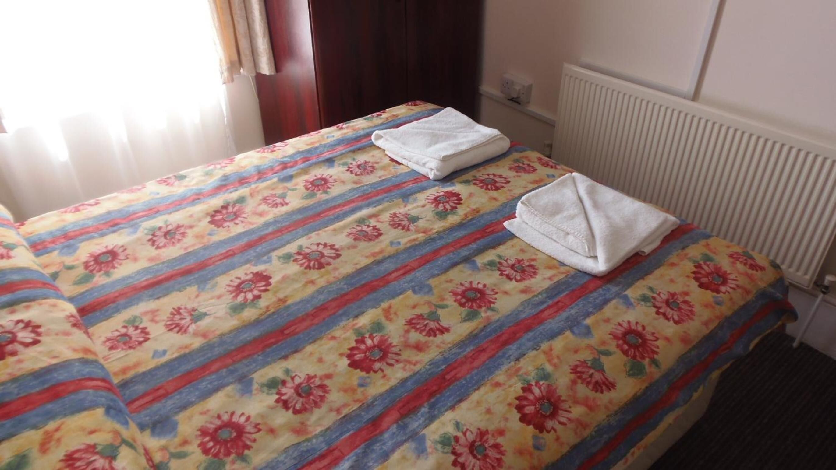 Habitación de hotel con dos camas, cada una con una colcha estampada de flores y una toalla blanca doblada.