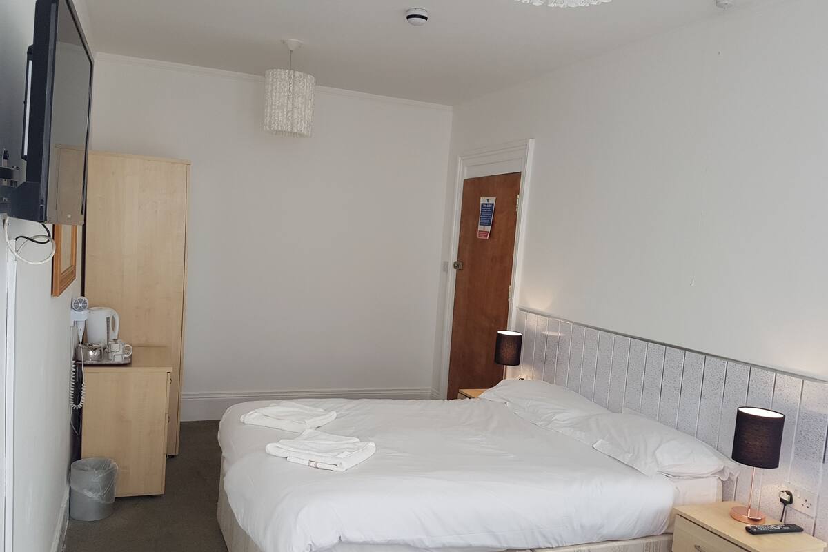 A hotel room with a bed, bedside table, lamp, and a wooden wardrobe.