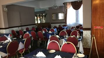 A dining area with tables set for multiple guests, red upholstered chairs, and a chandelier.