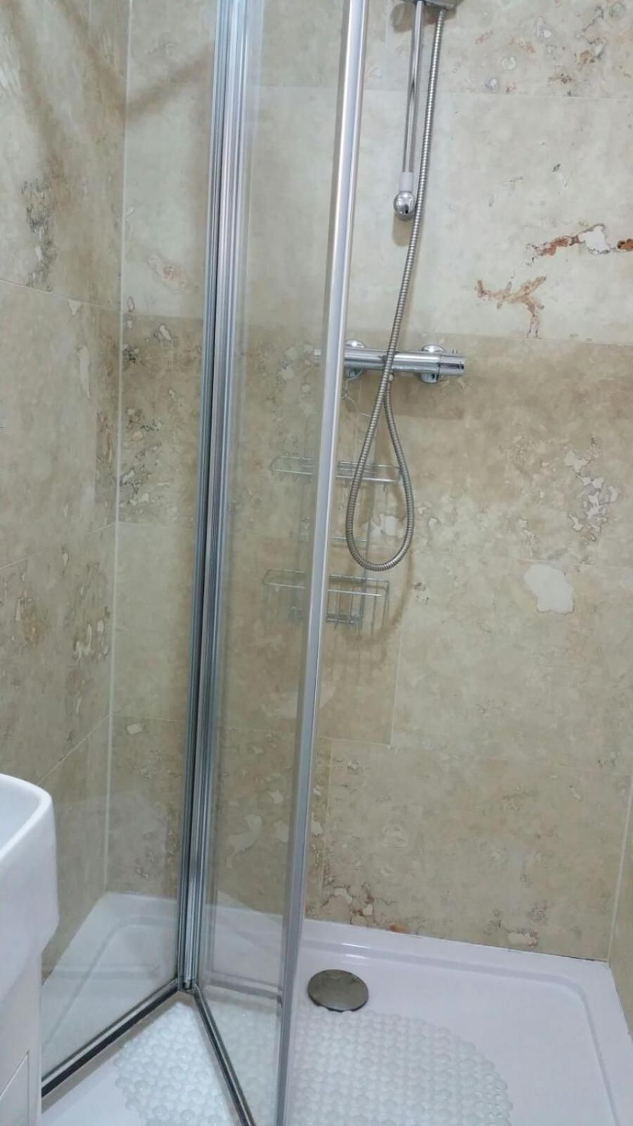 Un box de ducha con paredes de vidrio, un cabezal de ducha manual y un grifo empotrado.