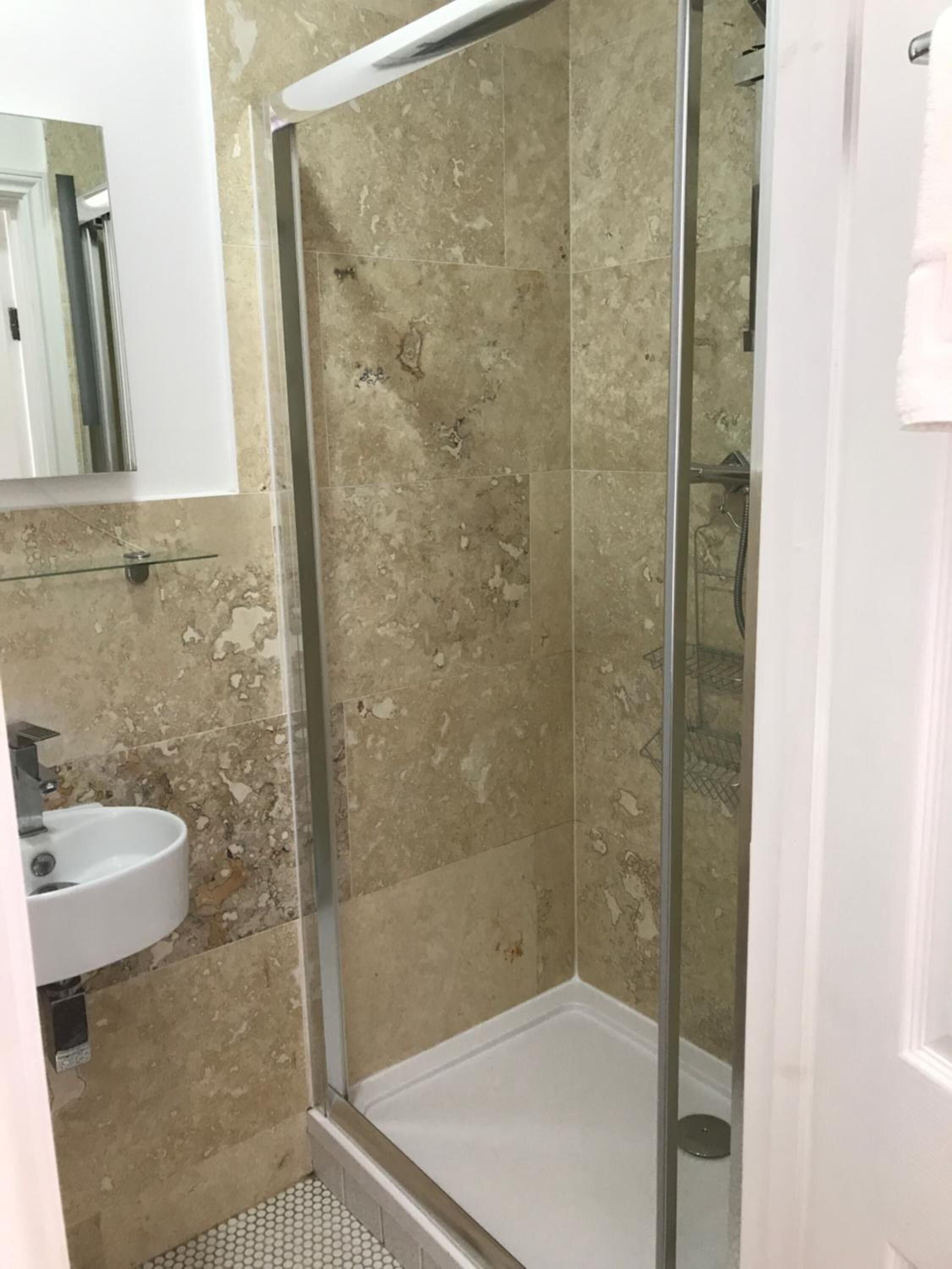 A bathroom with a glass shower enclosure, a sink, and a mirror.