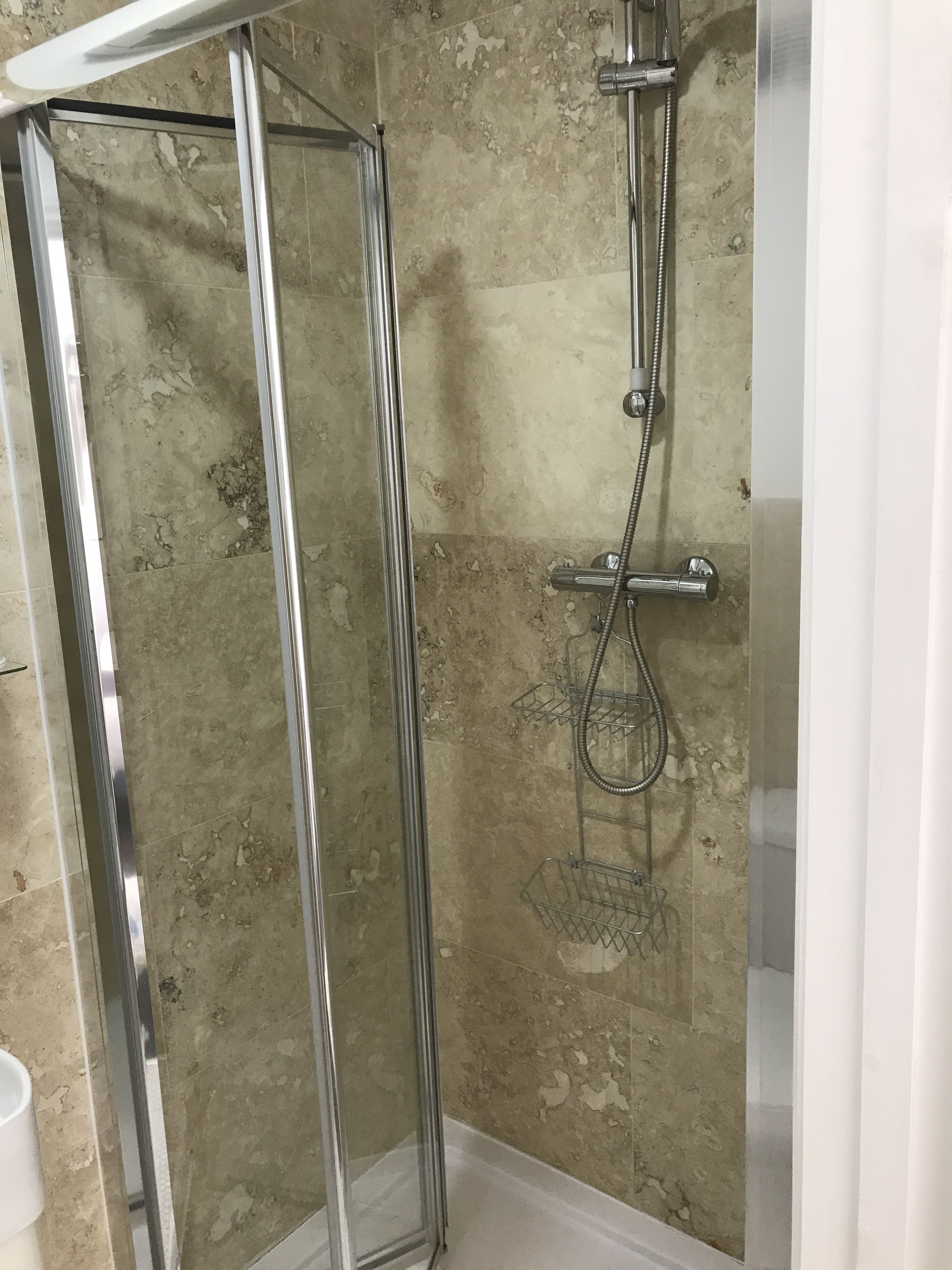 Ducha con cerramiento de vidrio, cabezal de ducha manual y llave de pared.
