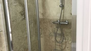 Ducha con cerramiento de vidrio, cabezal de ducha manual y llave de pared.