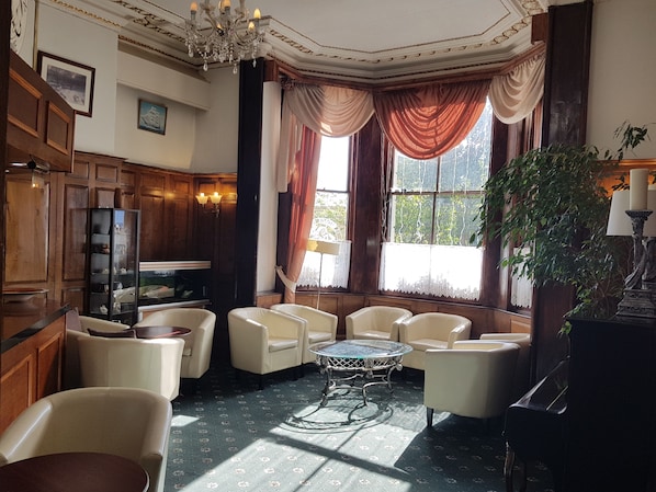 Ein Zimmer mit einer Kristallleuchtre, Holzvertäfelung, einem Kamin, einem Fernseher und einem großen Fenster mit Vorhängen.