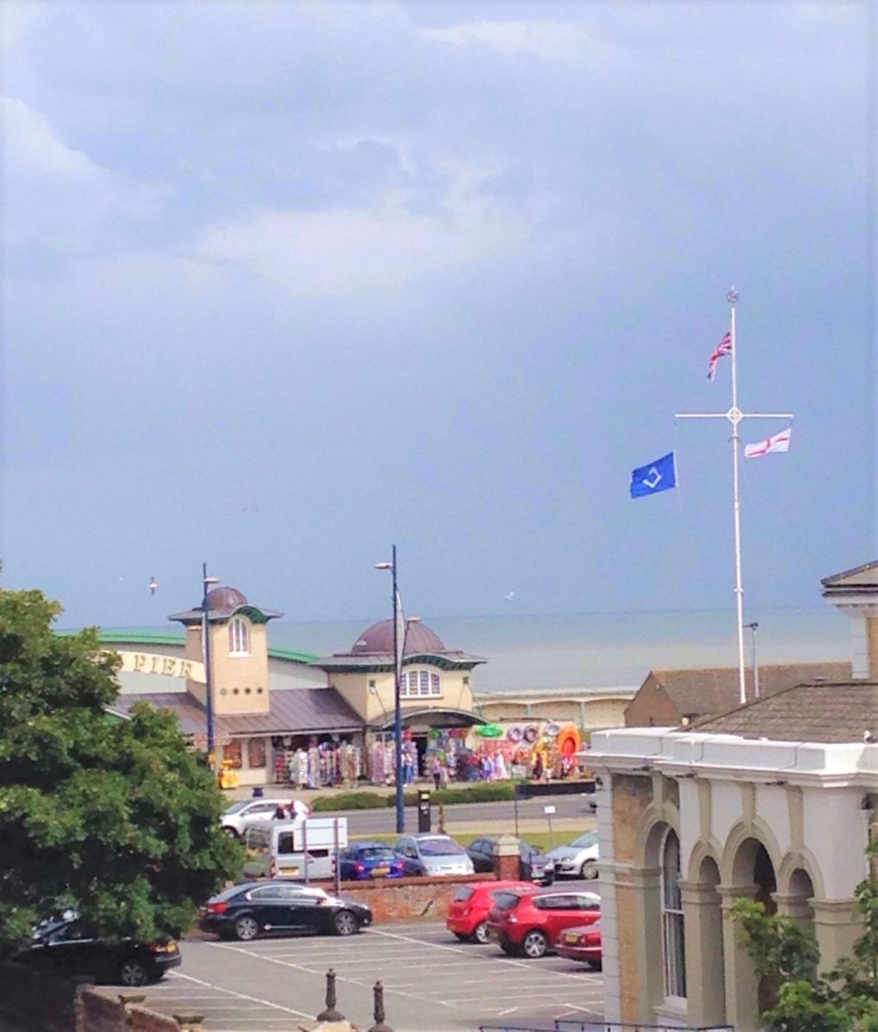 Une ville côtière qui se distingue par un bâtiment remarquable, sur lequel on peut lire l’inscription « Jetée », et par un mât sur lequel flottent des drapeaux.