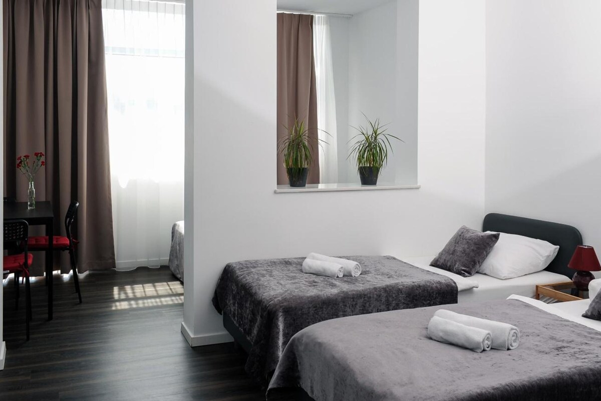 Habitación de hotel con dos camas, un escritorio con silla, una ventana con cortinas y un espejo.