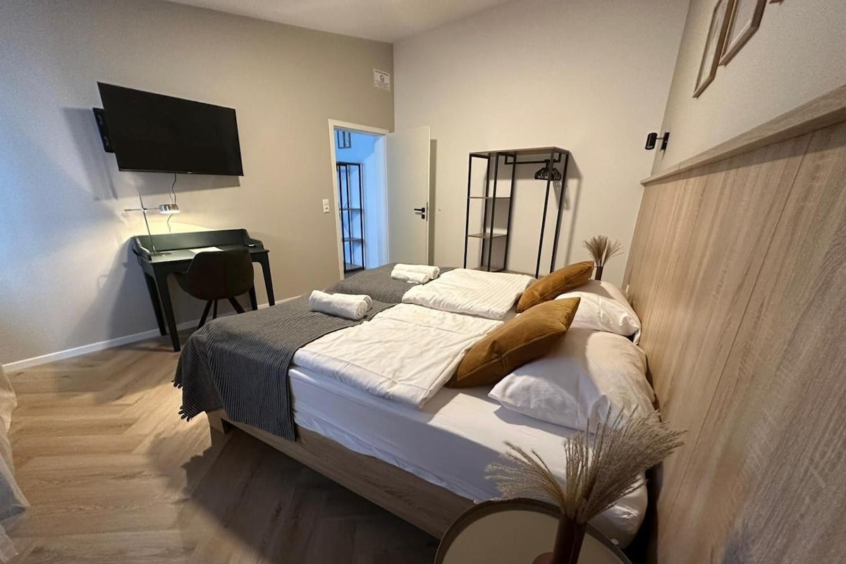 Ett sovrum med en säng, ett skrivbord, en stol, en tv och en dörr.