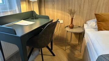 Hotelkamer met een bureau, stoel, nachtkastje, lamp en een bed met kussens.