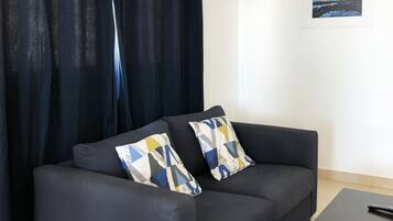 Un sofá oscuro con cojines estampados, una mesita y una cortina.