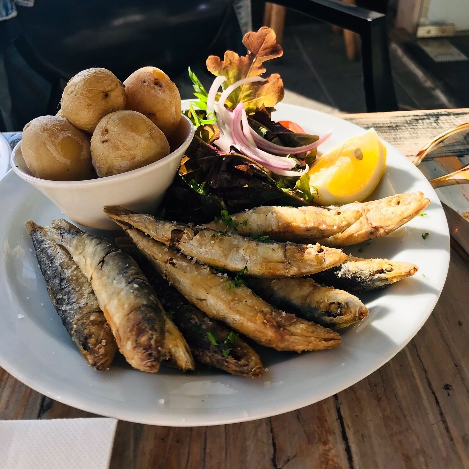 A plate of grilled fish, a bowl of potatoes, a lemon wedge, and a salad with red onion and greens.