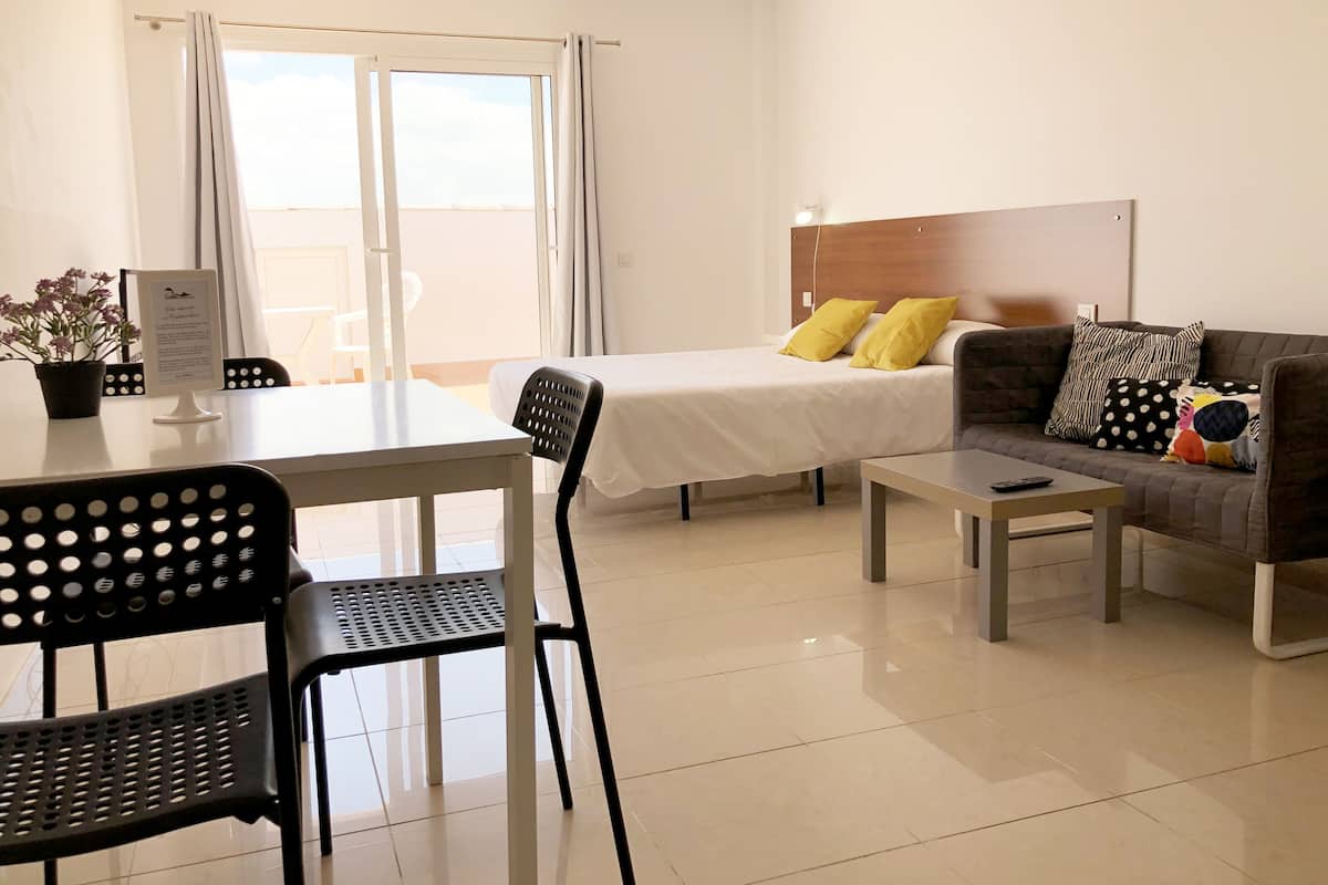 A modern hotel room with a bed, a sofa, a dining table, and a chair.