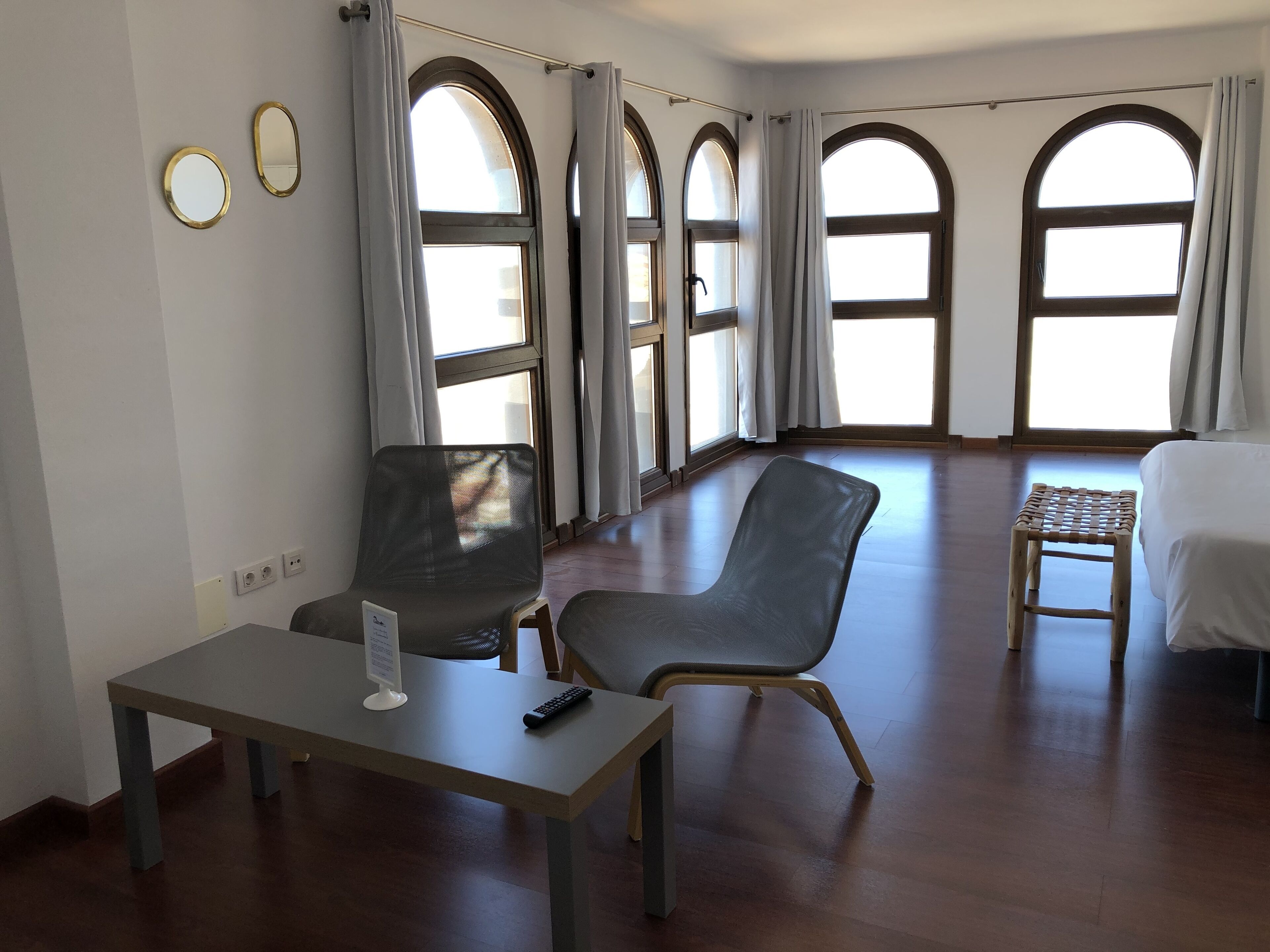 A hotel room with a large arched window, a bed, a desk with a chair, and a small table.