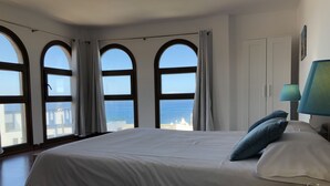 A bedroom with a large bed, a view of the sea through arched windows, and a lamp on the nightstand. - Cotillo Ocean View (La Oliva)