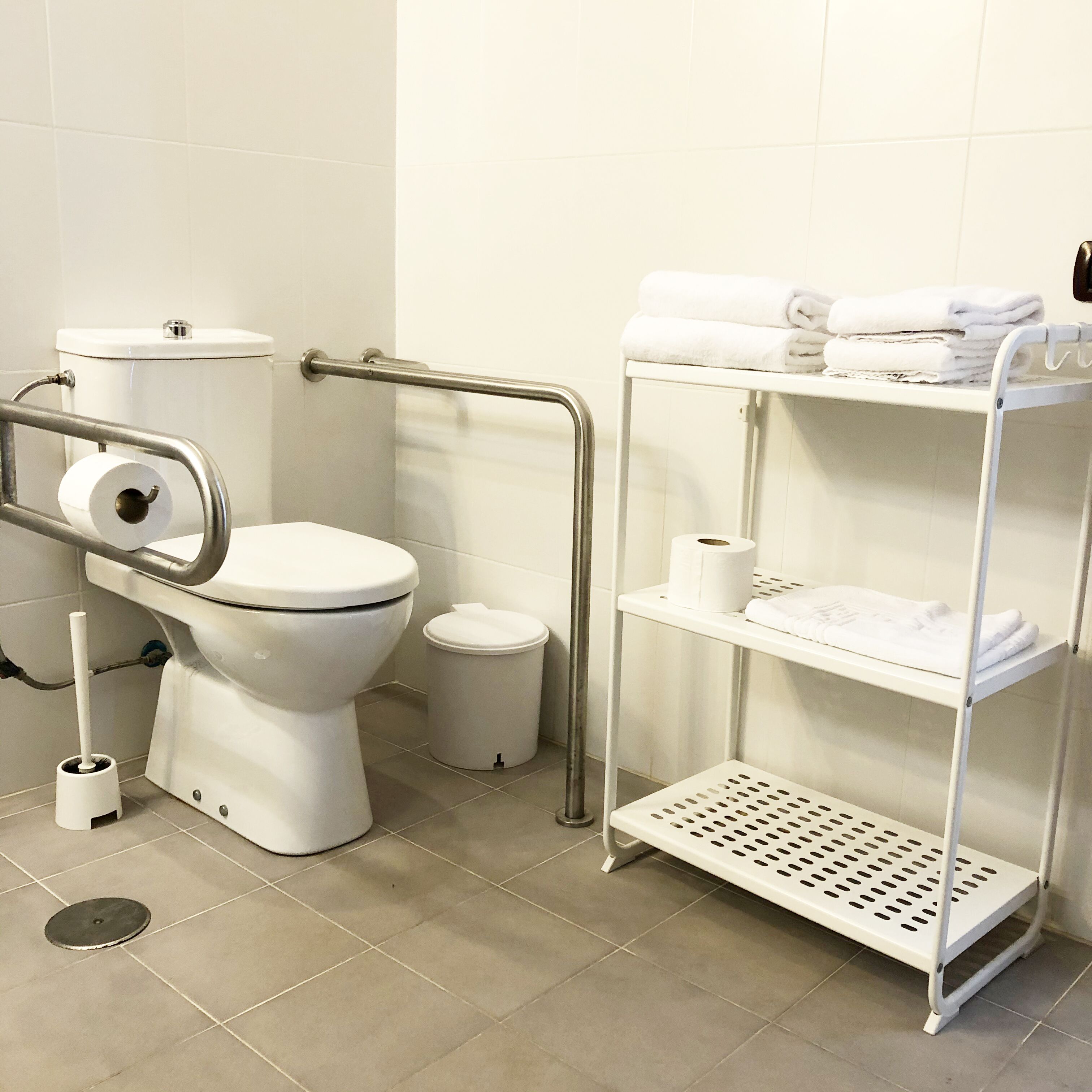 Une salle de bain équipée de toilettes, d’un sèche-mains, d’une poubelle et d’une étagère avec des serviettes.
