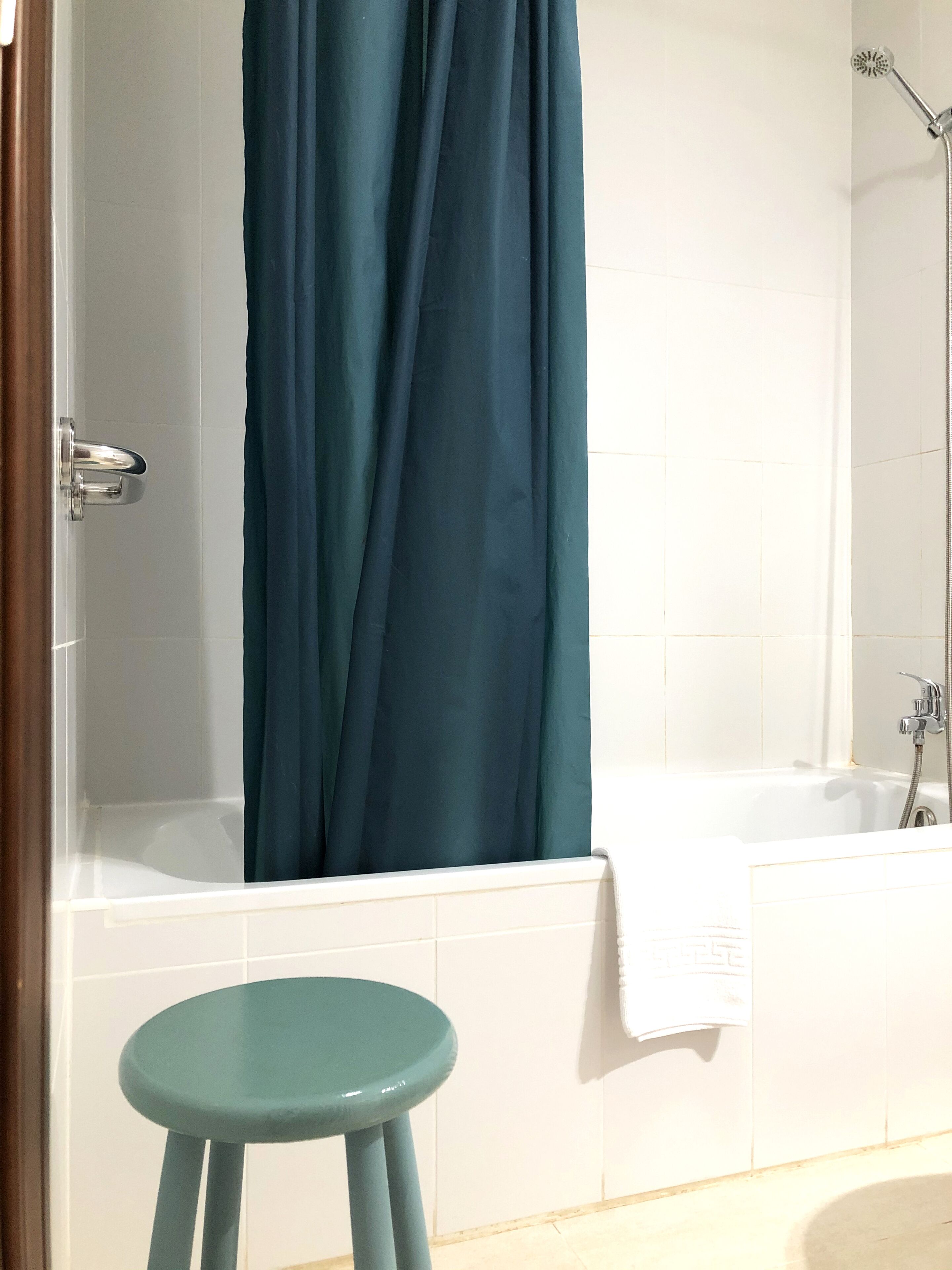 Un baño con bañera, ducha y un taburete verde.