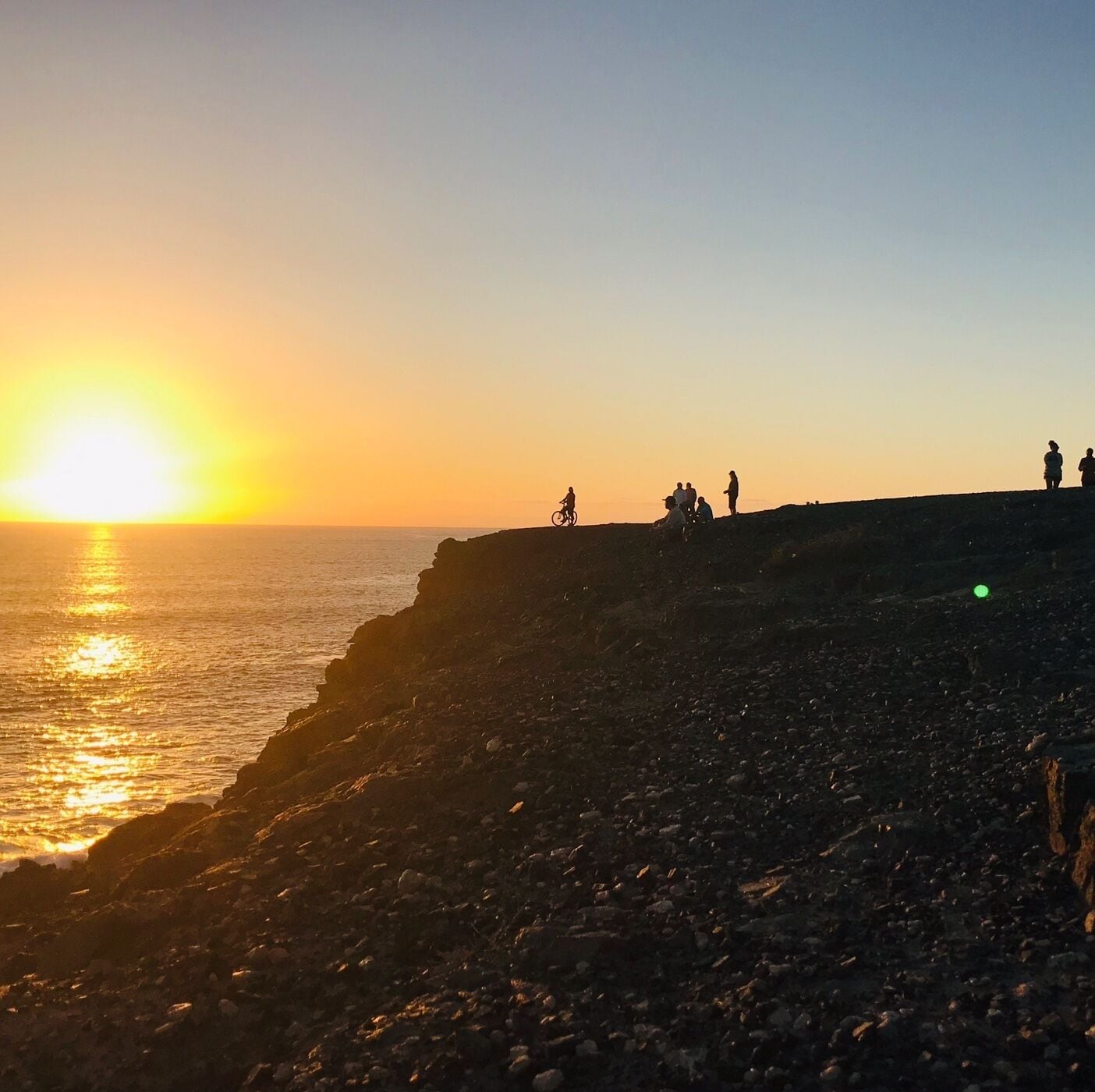Une plage rocheuse au coucher du soleil, avec des personnes et un vélo.