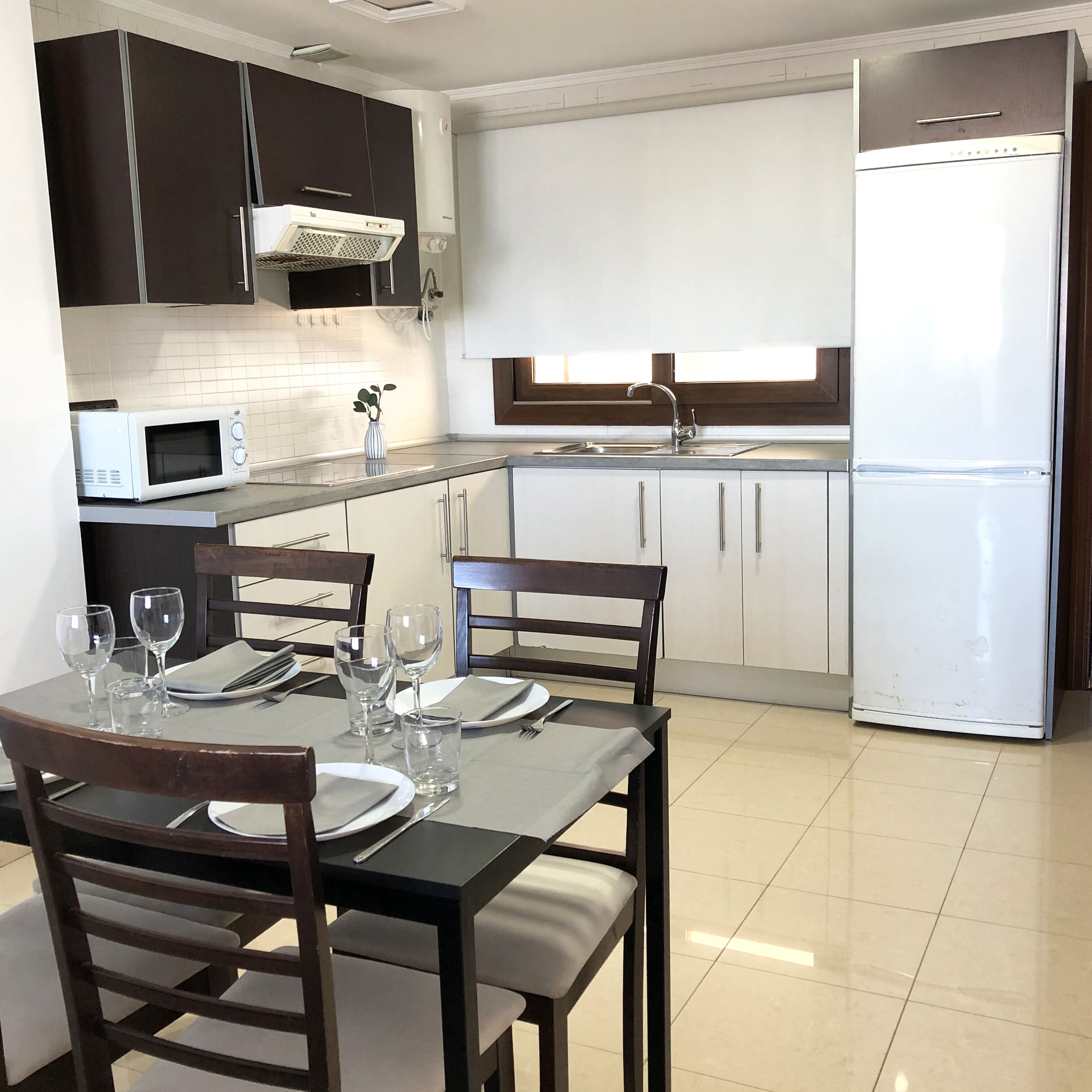 Una cocina moderna con armarios blancos, un refrigerador de acero inoxidable, un microondas y un lavabo.