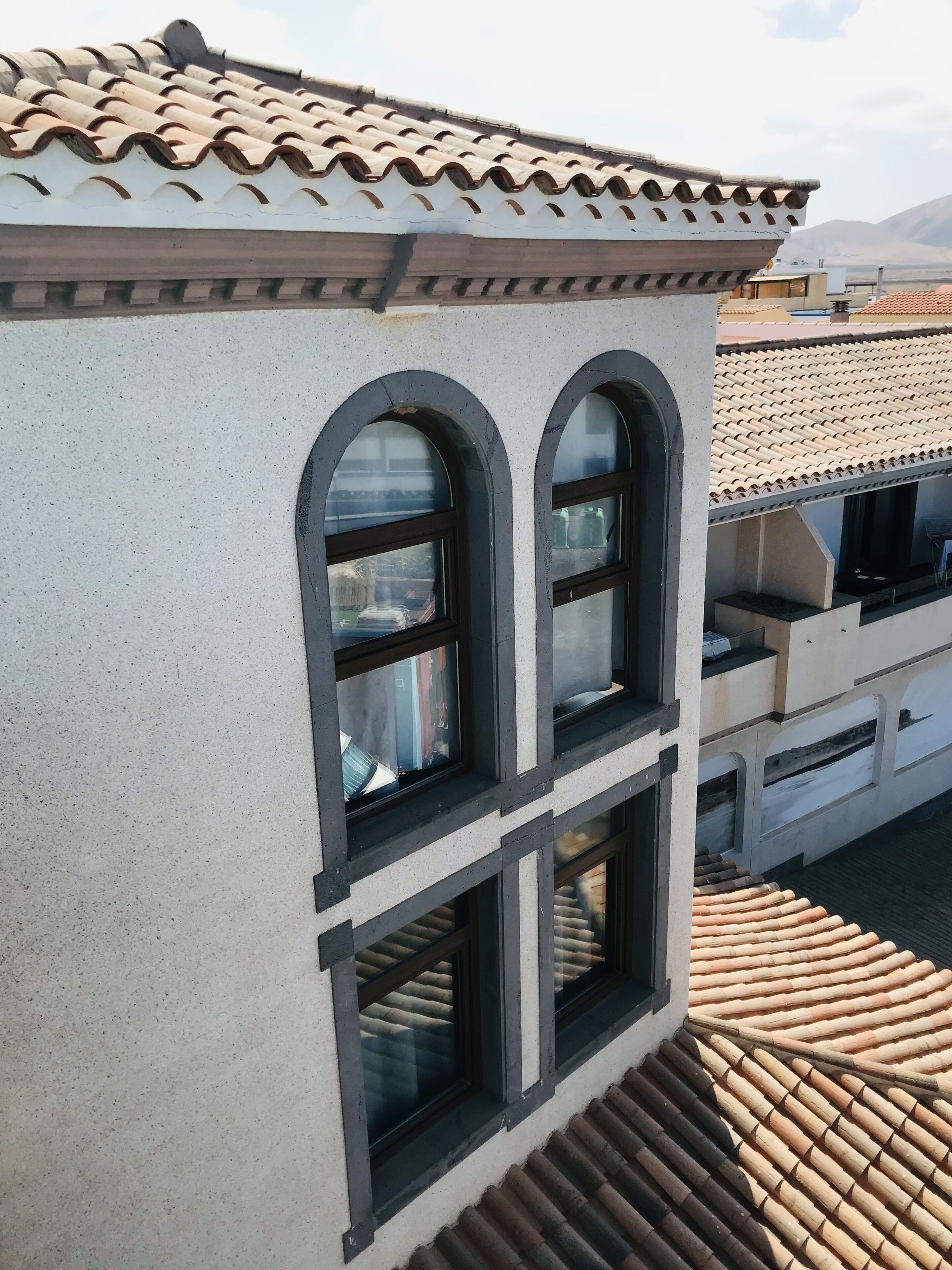 Un edificio con tejado de tejas, ventanas de arco y fachada de concreto.