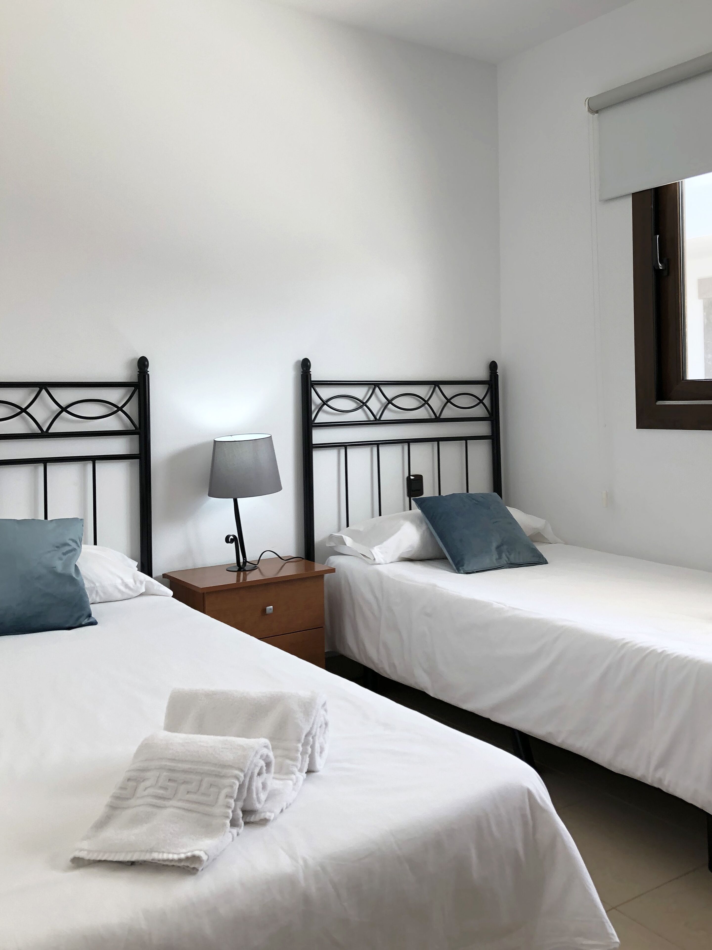 Una habitación de hotel con dos camas, una mesita de noche con lámpara y una ventana con cortina.