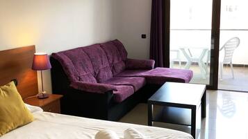 A hotel room with a bed, a sofa, a small table, and a balcony with chairs.