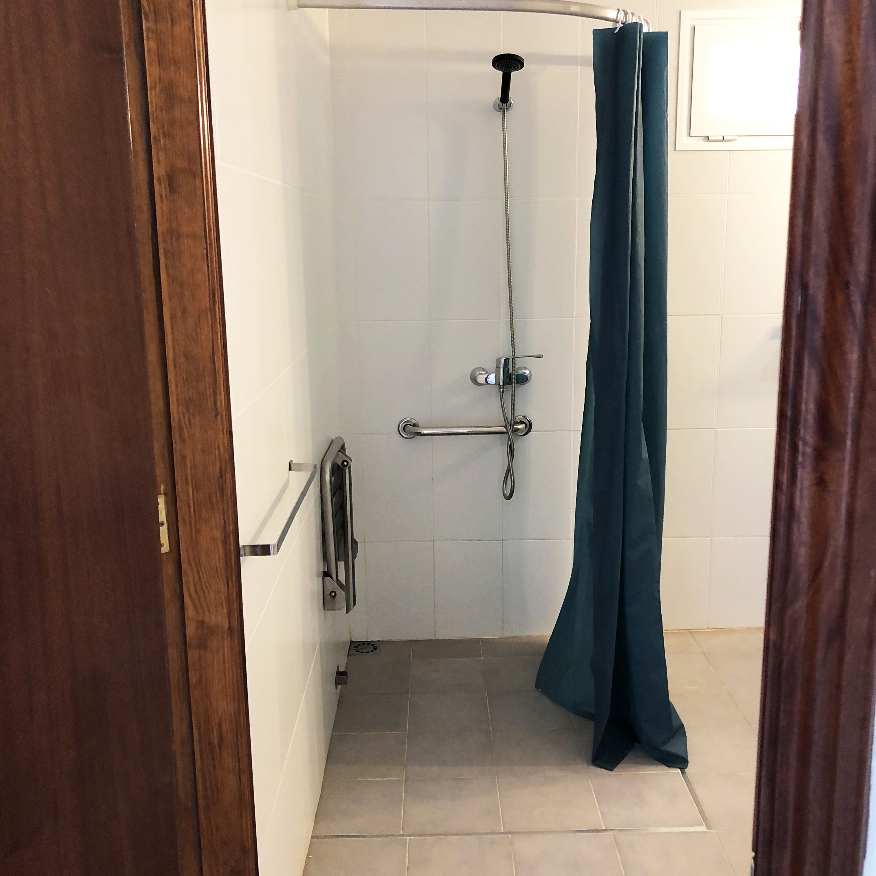 A small, enclosed shower area with a showerhead, a handheld shower attachment, and a dark green shower curtain.