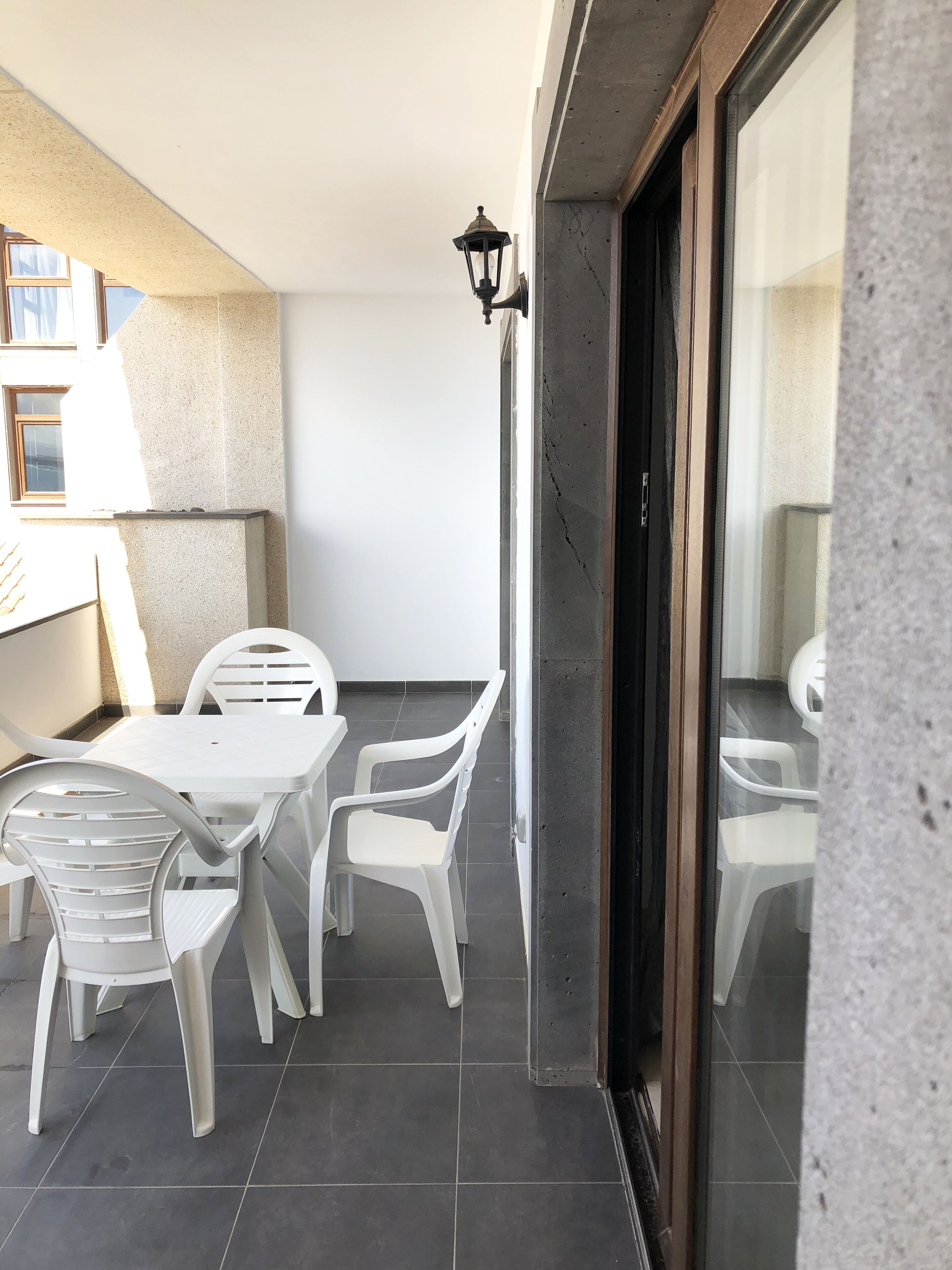 Ein Balkon mit weißen Plastikstühlen und einem Tisch, einer Topfpflanze und Blick auf das Meer.