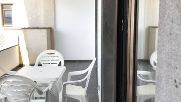 Ein Balkon mit weißen Plastikstühlen und einem Tisch, einer Topfpflanze und Blick auf das Meer.
