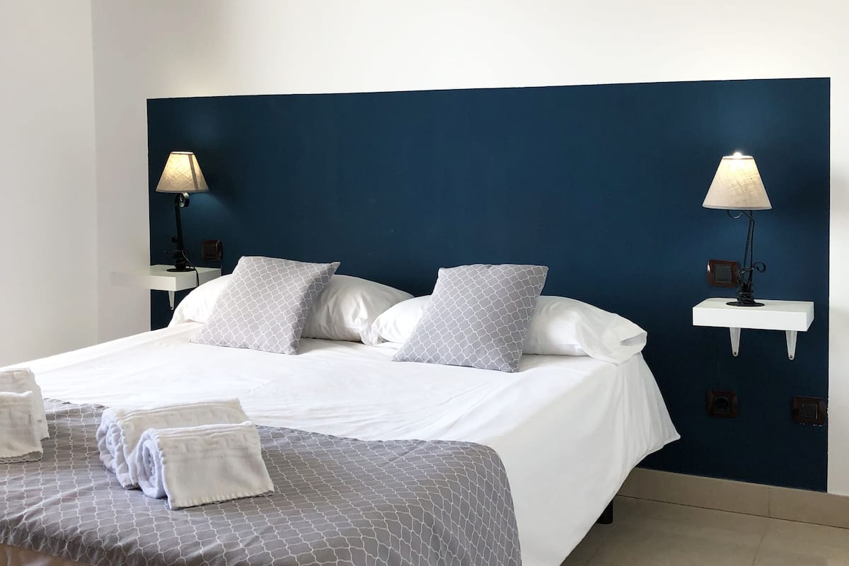 A neatly made bed with white linens, two bedside lamps, and a wooden chair.