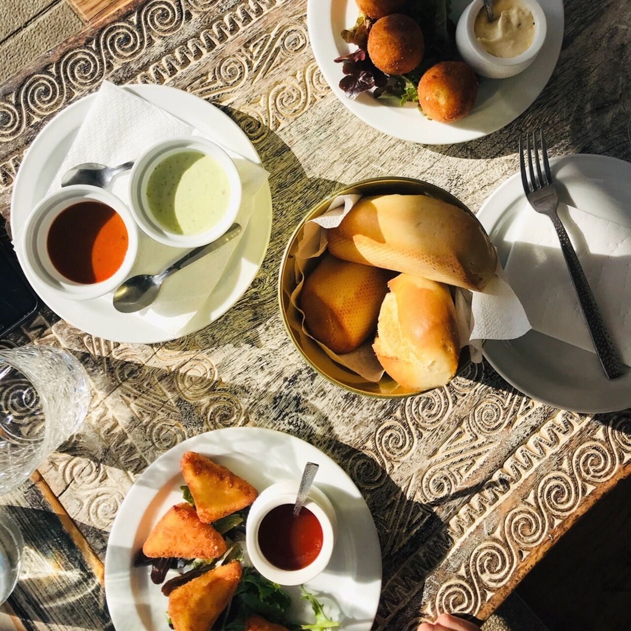 Et bord med forskellige retter, herunder rundstykker, friturestegte varme retter og to små skåle med saucer.