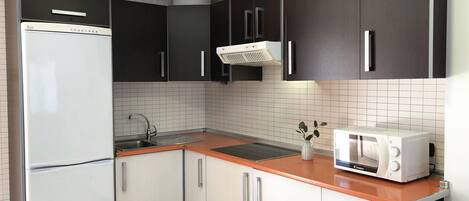 A compact kitchen with a refrigerator, microwave, sink, and cabinets.