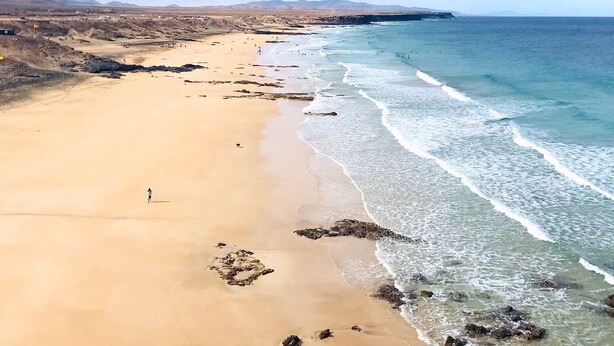 A wide sandy beach with gentle waves, a clear sky, and distant mountains. - Cotillo Ocean View (La Oliva)