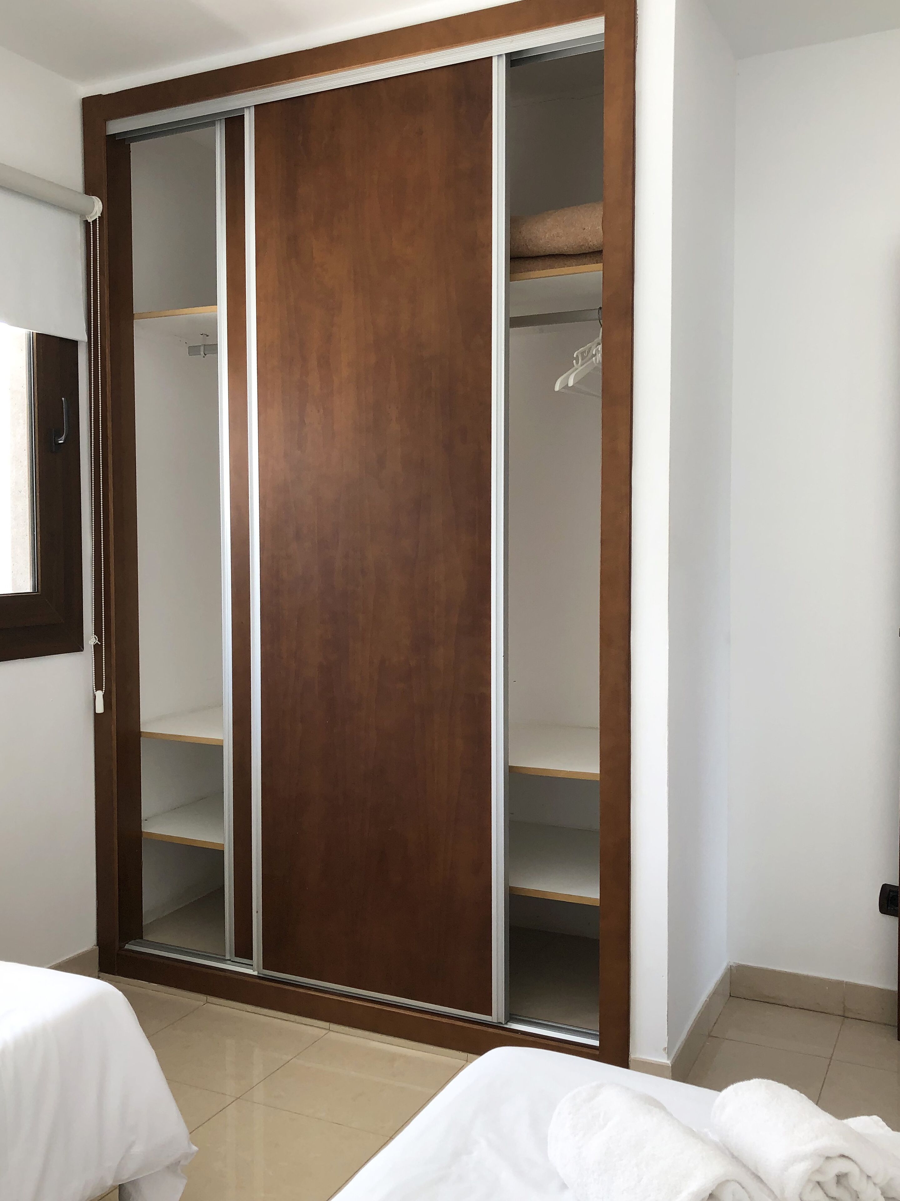 Een slaapkamer met een houten kledingkast, een bed en een bijzettafeltje.