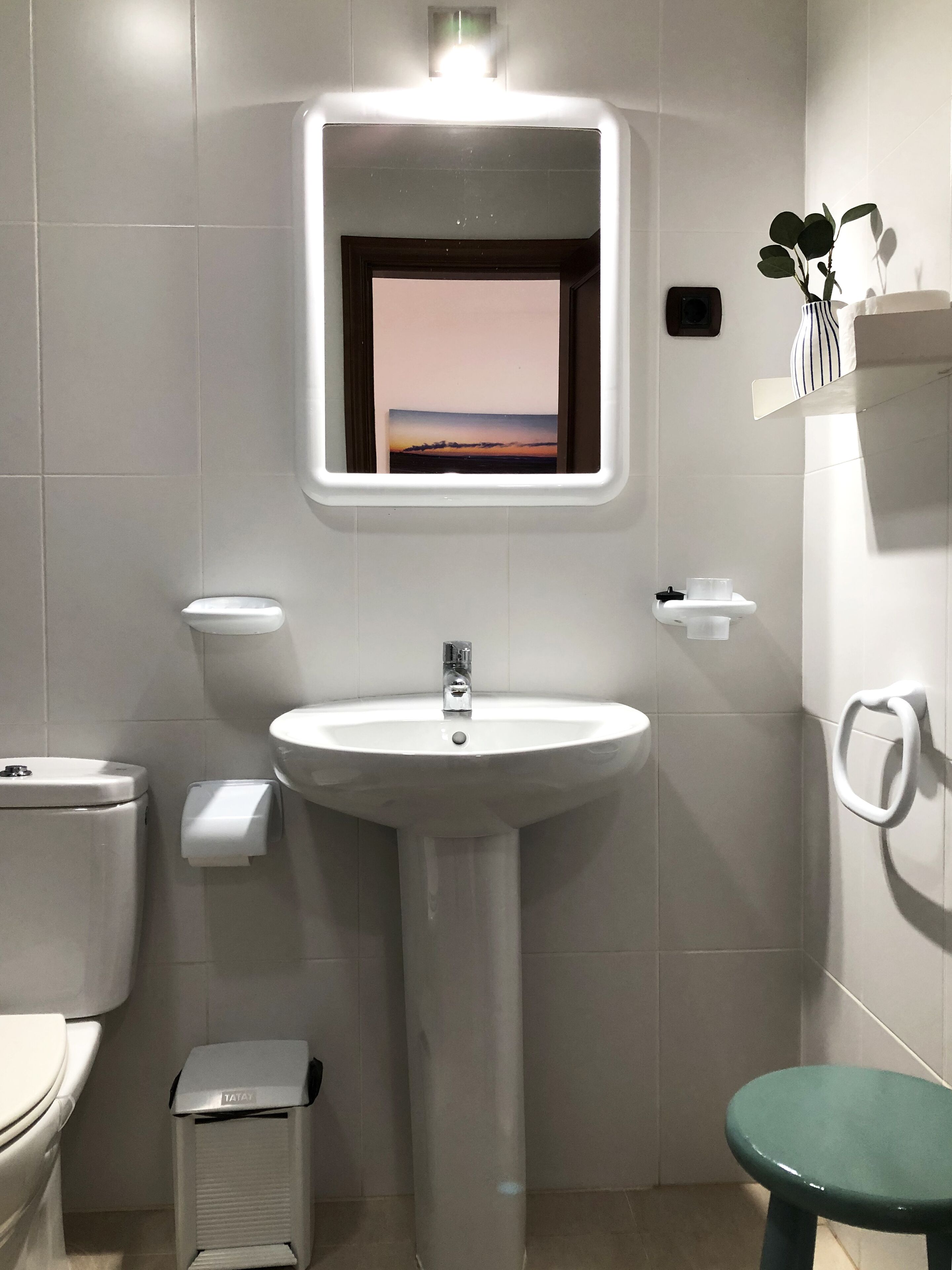 A modern bathroom with a white sink, toilet, and green stool.