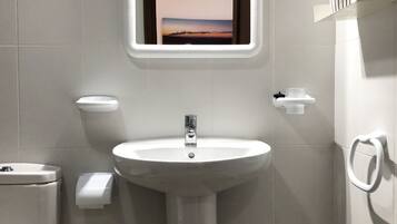A modern bathroom with a white sink, toilet, and green stool.